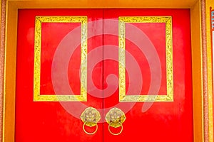 Golden door knocker in the shape of lion with ring on a red wooden door. Close up wooden Chinese style red door with lion head