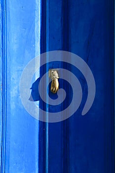 Golden doorknocker with hand shape on blue wooden door