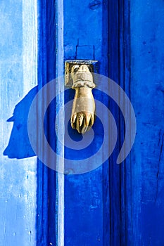 Golden doorknocker with hand shape on blue wooden door