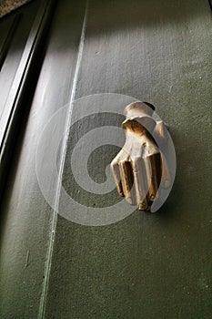 Golden doorknocker with hand shape on old green wooden door