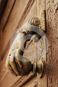 Golden doorknocker with hand shape on old wooden door