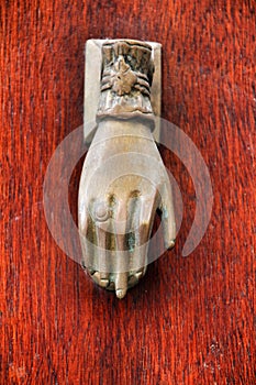 Golden doorknocker with hand shape on old wooden door