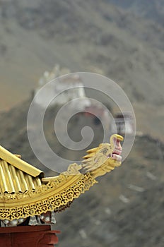 A golden dragon`s head on the corner of a shrine, with a temple and mountains in the background