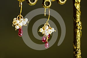 Golden earrings with red rubies with white pearls on black background.
