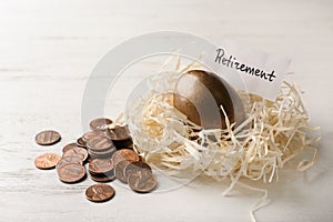 Golden egg and card with word RETIREMENT in nest near coins on wooden background