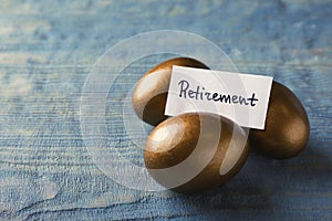 Golden eggs and card with word Retirement on wooden background, space for text