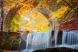 Golden Fall Autumn landscape - river waterfall in colorful autumn forest park with yellow red leaves with old bridge