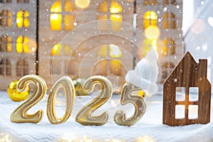 Golden figures number 2025 and tiny home on background of cozy windows of a house with warm light with festive decor of stars,snow