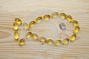 Golden fish oil capsules, on wooden background, fish made of translucid capsules.