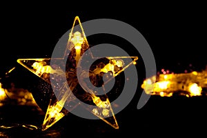 A golden five-pointed star, shining against the background of bokeh and blurred lights of garlands.