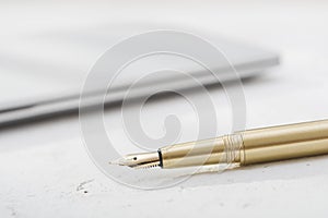 Golden fountain pen with blurred notebook on vintage desk surface