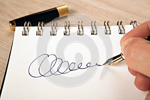 Golden fountain pen in the hand and a signature on the paper