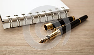 Golden fountain pen near the notepad with paper closeup