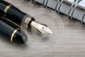 Golden fountain pen near the notepad on a wooden table