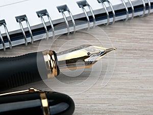 Golden fountain pen near the notepad on a wooden table