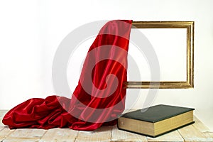 golden frame unveiled by a red satin curtain over a green thick book