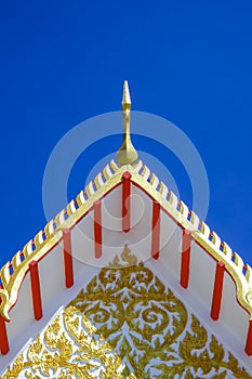 Golden gable apex on ornamental Thai temple roof against blue clear sky background