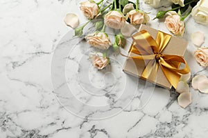 Golden gift box and beautiful roses on white marble background, flat lay. Space for text
