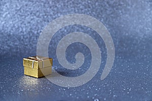 Golden gift box on blue sparkling glittery background. Photo with selective focus. Backdrop with copy space