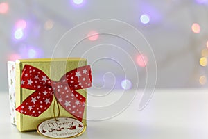 Golden Gift box with red bow and defocused christmas lights on the background