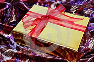 Golden gift box with red bow over colorful velvet