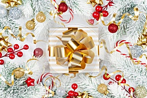 Golden gift or present box, snowy fir tree and christmas decorations on white wooden table top view. Flat lay.