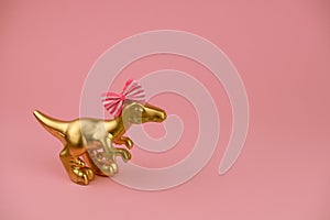 golden girl dinosaur toy with festive bow on a sift pink background with copy space