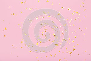 Golden glitter confetti sparkles on pastel pink background. Flat lay, top view. Holiday, festive, party backdrop.