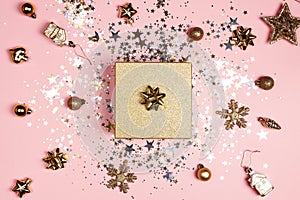 Golden glittering gift box with Christmas decorations and sparkling sequins all around on pink background