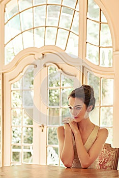 Golden glow beauty. Shot of a beautiful young woman sitting at a table in her elegant home.