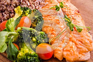 Golden grilled fish fillet with a side dish of rice and vegetables on a wooden board on a white background