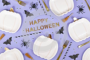 Golden Happy Halloween text surrounded by pumpkin shaped plates, witch brooms, spiders and bats