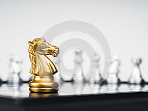 The golden horse, knight chess piece stand alone in front of silver chess pieces on chessboard.