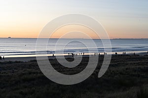 Golden hour sunrise over Mount Maunganui ocean and beach with incidental people in distance and in silhouette