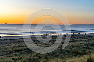 Golden hour sunrise over Mount Maunganui ocean and beach with incidental people in distance and in silhouette