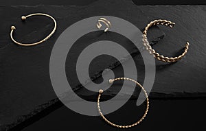 Golden jewelries three bracelets chain and spiral shape and ring on black stone surface