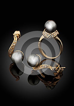Golden jewelry set with pearls on black background with reflection
