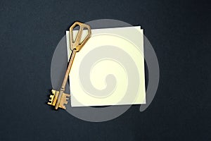 A golden key on a piece of note paper. Wish list, problem solution, idea, decoding, business concept on a black background with a