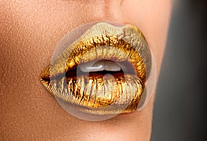 Golden lipstick closeup. Metal gold lips. Beautiful makeup. Sexy lips, bright paint on beautiful model girl`s mouth, close-up