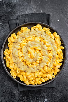 Golden mac and cheese in a black skillet, rustic dark background, fork beside