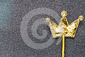 Golden magic stick from sequins in crown shape on black glitter background. Creative flat lay close up