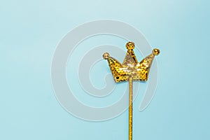 Golden magic stick from sequins in crown shape on pastel blue background. Creative flat lay in minimal style