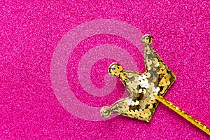 Golden magic stick from sequins in crown shape on pink glitter background. Creative flat lay close up