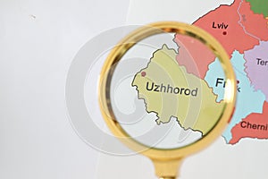 Golden magnifying glass above Uzhhorod region on map of Ukraine, closeup