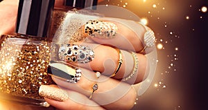 Golden manicure with gems and sparkles. Bottle of nailpolish, trendy accessories photo