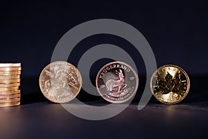 A golden Maple Leaf coin lies next to a Krugerrand coin and a gold dollar