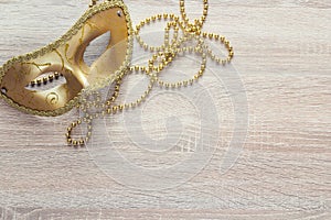 Golden Mardi Gras masks and beads on a wooden background.