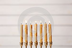 Golden menorah with burning candles on light background, space for text