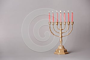 Golden menorah with burning candles on light grey background, space for text