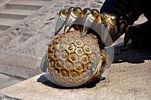 Golden metallic sculpture with one foot securely placed atop a bright yellow round ball